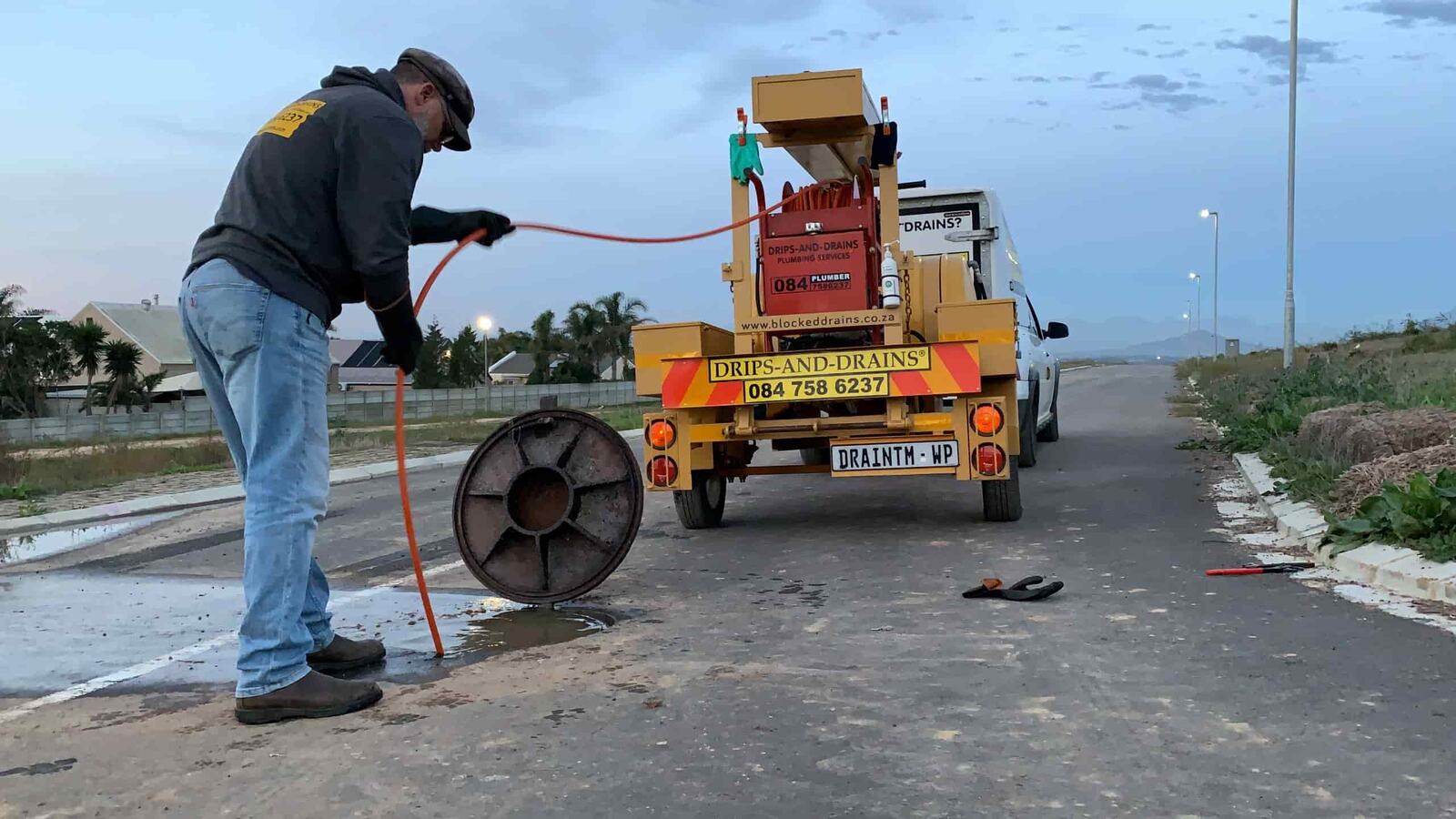 Drips-and-Drains plumber hydro-jetting a blocked sewer line with a trailer-mounted jetter