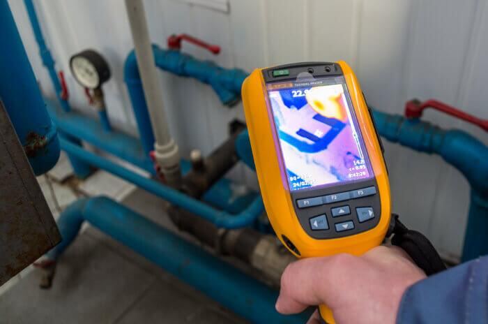 Plumber using a thermal imaging camera to trace a leaking water pipe